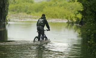 What is the main reason it is a bad idea to bike through flooded streets and puddles?