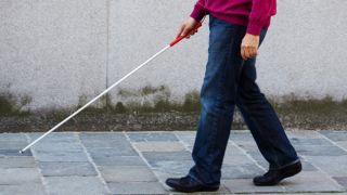 You see a pedestrian carrying a white cane crossing the road. What should you do?