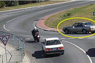 The motorcyclist wants to travel straight ahead through this roundabout. The rider should watch out for the marked car because the car: